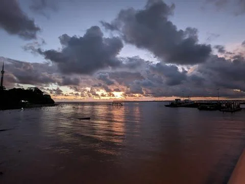 Waterfront sunset with dramatic clouds, pier, and boats along shoreline Foto stock
