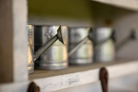 Watering Cans lined up on a shelf Stock Photos