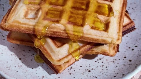 Watering soft waffles with bee honey during dessert cooking, making sweets from Stock Footage 303631903