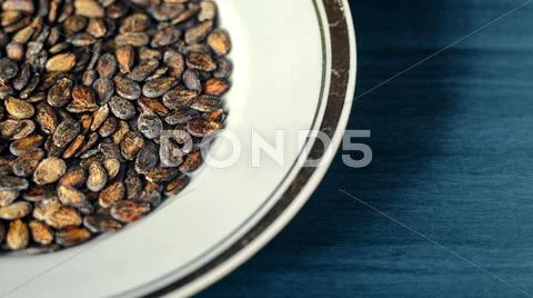 Watermelon seed kernels in a white dish with a gold borders on wood deep blue b Stock Photos