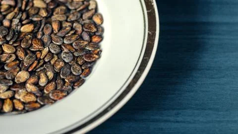 Watermelon seed kernels in a white dish with a gold borders  on wood deep blue b Stock Photos
