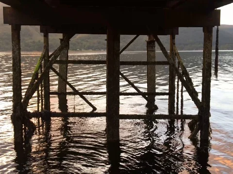 Waters flow and ripple underneath the wooden dock of Loch Sunart 4K as the sun Stock-Footage 79884932