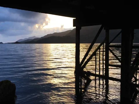 Waters flow and ripple underneath the wooden dock of Loch Sunart 4K as the sun Stock-Footage 79884940