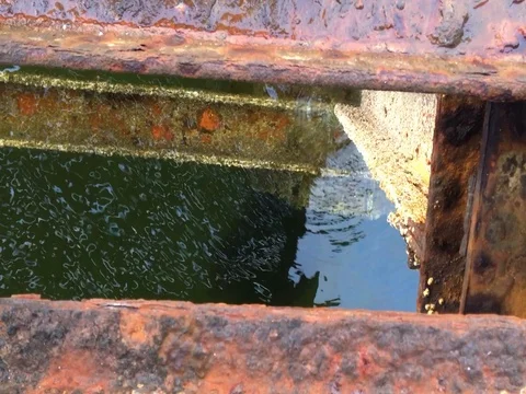 Waters flow beneath the rusting weather stained bars of an old dock Stock-Footage 79884898