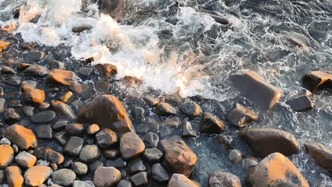 Wave action contrasts with rough volcanic rock textures. Dynamic sea foam Stock Footage 323362465