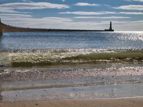 Wave breaking in the foreground of a distant Roker Lighthouse, Sunderland, UK Stock Photos