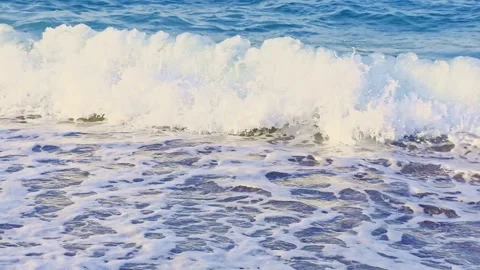 Wave breaking onto a Mediterranean shoreline with white foam spreading acro.. Video stock 338133083