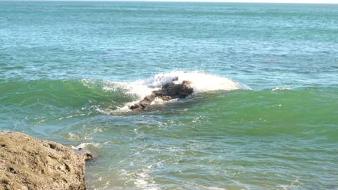 A wave crashes over a rock in the turquoise ocean water under bright sunlight-83 Stock-Footage 345519776
