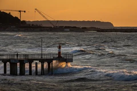 Wave crashes on the pier, wind waves in the Baltic Sea, at sunset Stock Photos