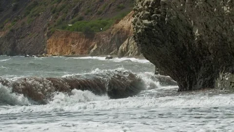 The wave crashes into the rock, darting out the trail time after time in slow Stock Footage 217864258