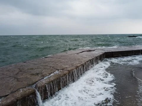 The wave rolls over a large square rock lying on the shore, covered with green Foto stock
