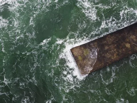 The wave rolls over a large square rock lying on the shore, covered with green Foto stock