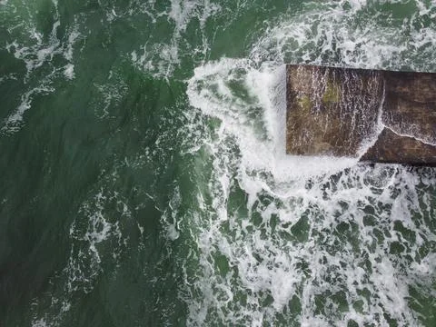The wave rolls over a large square rock lying on the shore, covered with green Stock-Fotos