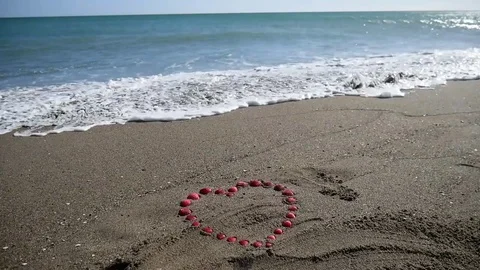 The wave rolls on the sand red shells. Heart made of red shells. Vídeos de archivo 72966384