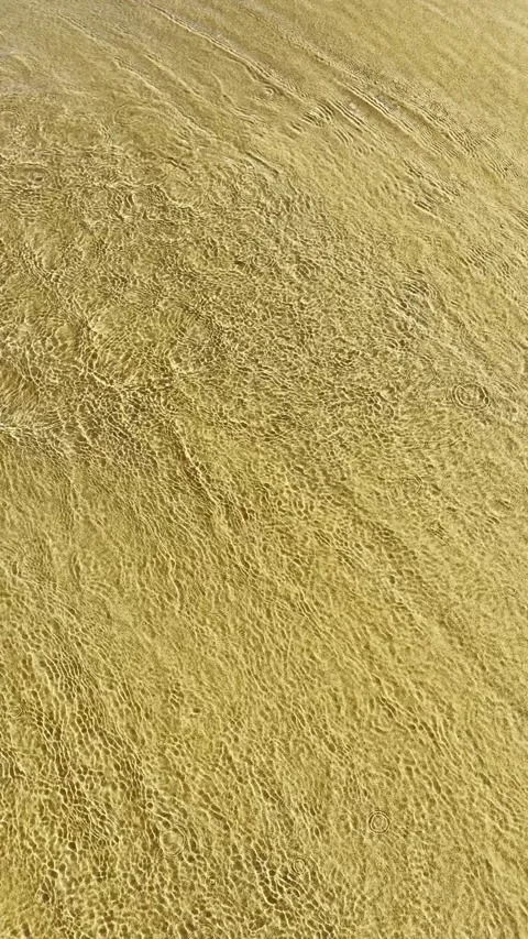 The wave rolls onto the yellow sand, forming unique patterns. Video stock 343537260