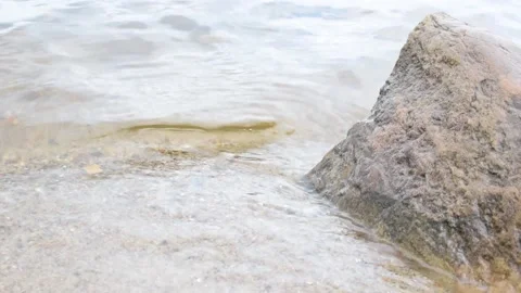 A wave on a sandy shore beats against a large stone Stock Footage 198688802