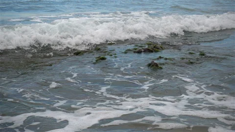 Wave in slow motion rolls onto a sandy stone beach Video stock 122561331