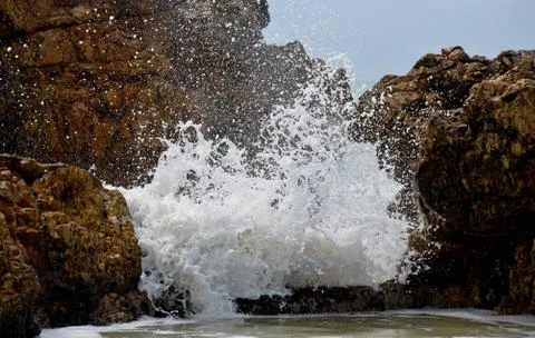 Wave splashes through rocks into rock pool Stock Photos