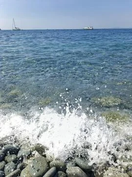 Wave splashing on a pebble beach with clear blue sea water Stock Photos