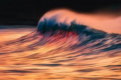 Wave with spray breaking at sunset with in camera panning technique Stock Photos