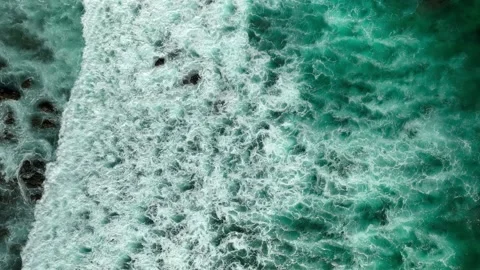 Wave texture from overhead foam rolling into rocky shore Stock Footage 236741944