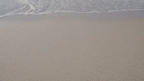 A wave washes away footprints on a sandy beach. feet guy in the frame Stock Footage 119884558