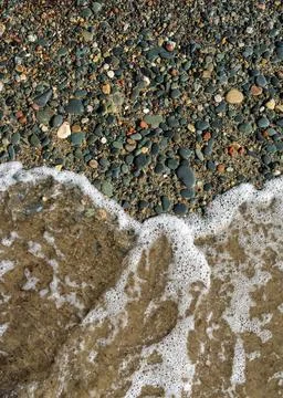 Wave with white foam softly lapping against pebble shoreline. Tranquil beach  Stock Photos