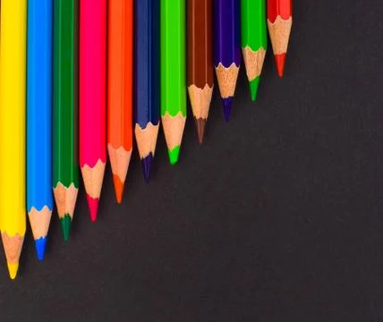 Waved row of different colored pencil crayon placed on top of a black colored Stock Photos