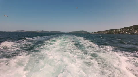 Waves after a steamship with seagulls flying behind it against a blue cloudy sky Stock Footage 280398965