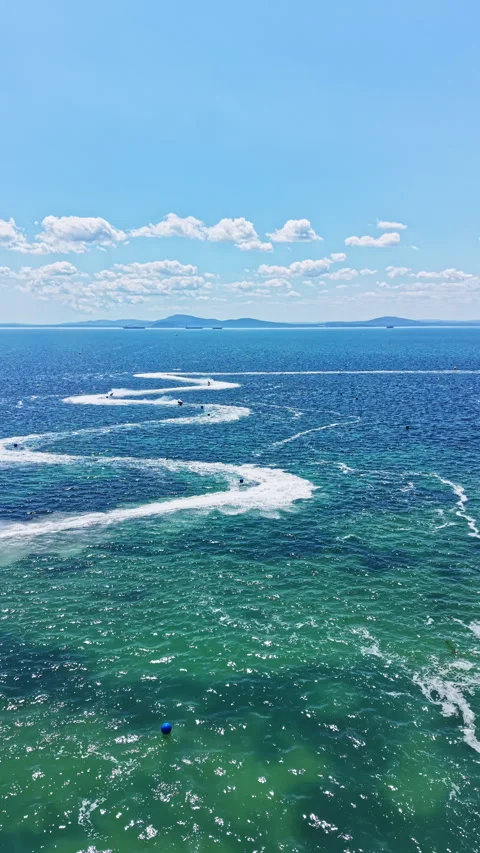 Waves and boats create trails in blue water under clear sky near coastal Stock Footage 346982490