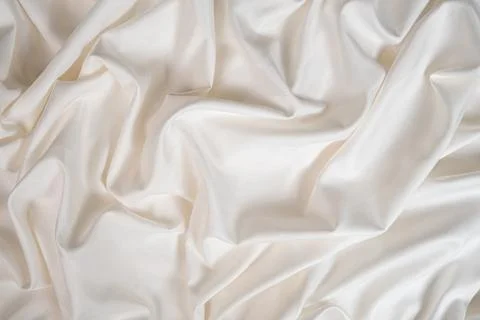 Waves and patterns of crumpled natural satin white milk color fabric. Stock Photos