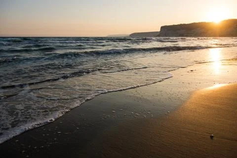 Waves approaching sandy beach during the sunset Stock Photos