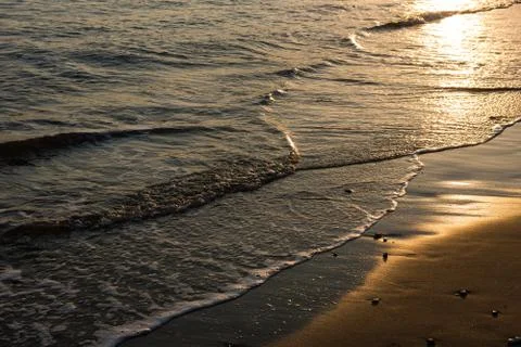 Waves approaching sandy beach during the sunset Stock Photos