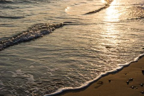 Waves approaching sandy beach during the sunset Stock Photos