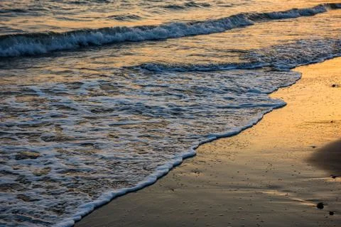 Waves approaching sandy beach during sunset Stock Photos