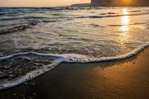 Waves approaching sandy beach during sunset Stock Photos