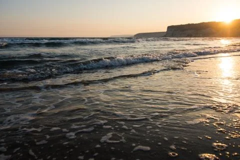 Waves approaching sandy beach during the sunset Stock Photos