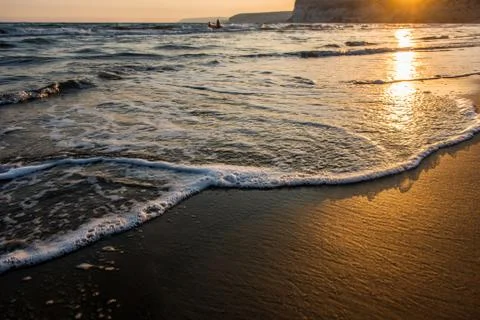 Waves approaching sandy beach during the sunset Stock Photos