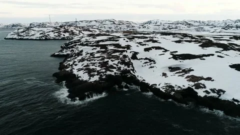 Waves of the Arctic Ocean beat against a rocky shore covered with snow. Town on Stock Footage 169464378