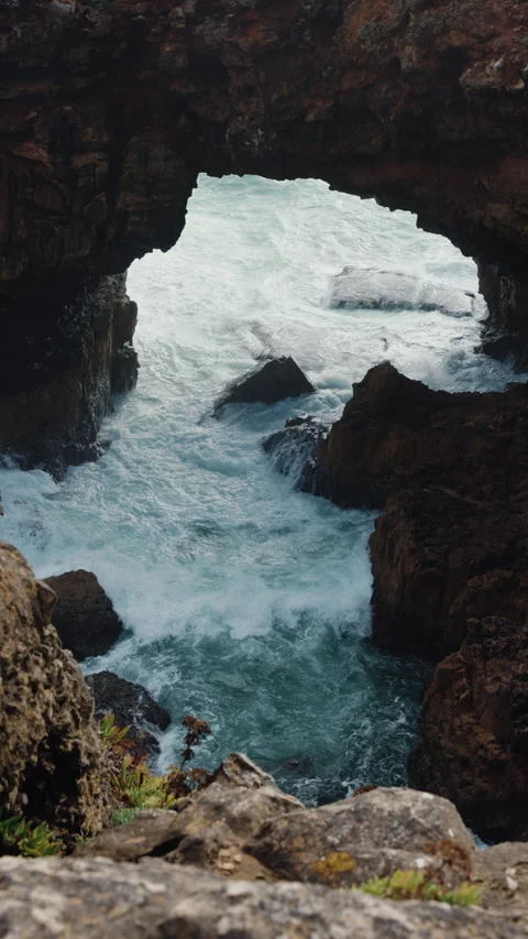 Waves are crashing dramatically through the rocky arch that stands majestically Stock Footage 303889186