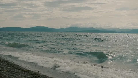 Waves of bay sparkling in sun roll onto sandy shore and view of green mountain Stockbeeldmateriaal 318671092