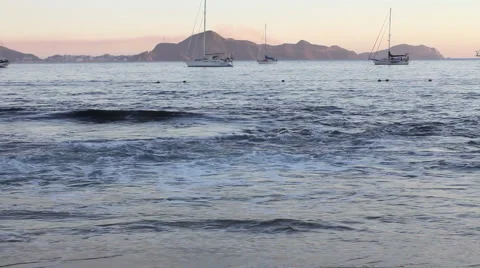 Waves on beach with sailboats at sunset Stock Footage 1072144