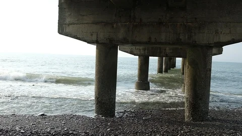 Waves beat against the pillars of a concrete pier. Video stock 128798890