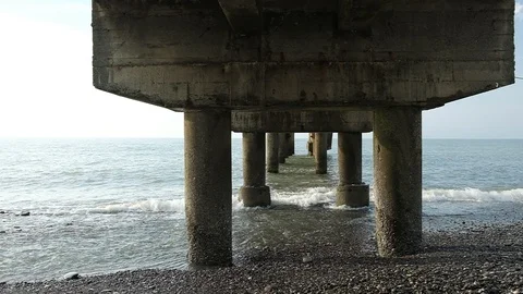 Waves beat against the pillars of a concrete pier. Video stock 128799414