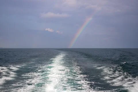 Waves from a boat sailing with rainbow in the backdrop in andaman sea off the Stock Photos