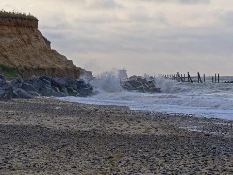 Waves break on rocks protecting soft Norfolk cliffs from erosion Stockfoto's
