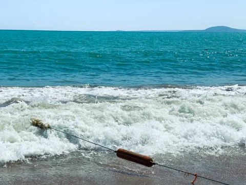 Waves break on the sandy beach during the day. A rope extends into the water, Stock Photos