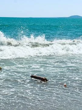 Waves break on a sandy beach near a wooden object in the water. A distant isl Stock Photos
