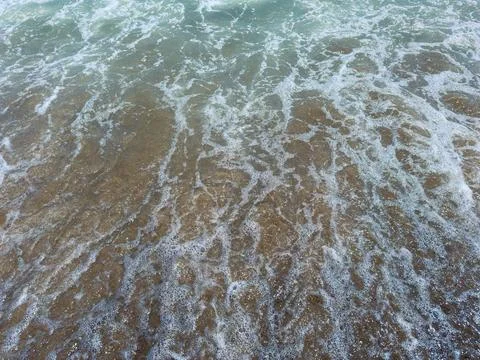Waves break on sandy shore as sunlight reflects on water surface in a coast.. Stock Photos