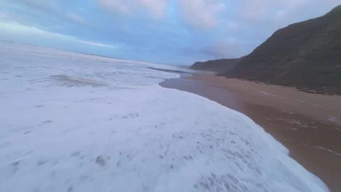 Waves break on shore with seaweed, mountains rise in background Stock Footage 344673887